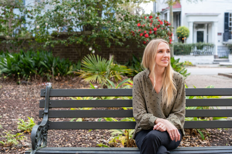 Image shows art therapist Katie Hinson Sullivan, a smiling woman with long blonde hair, sitting on a park bench.