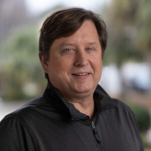 Headshot of Wade Sellers, a white male with wavy dark brown hair parted on his left side.