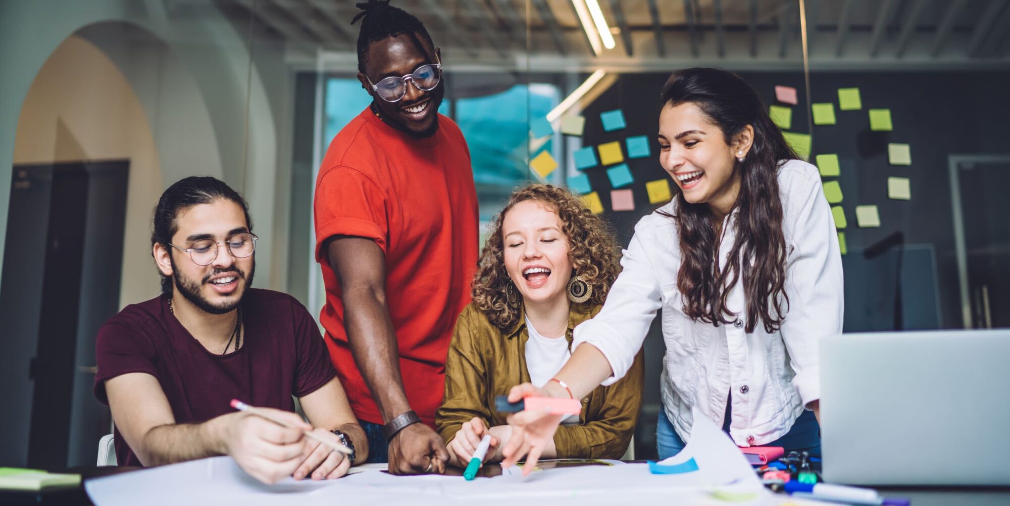 A group of young entrepreneurs of different races and sexes huddle around a table working on a project.