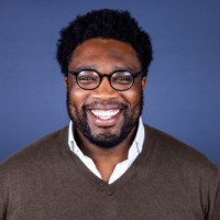 Headshot of Ace Callwood, a black man with medium length hair wearing dark rimmed glasses