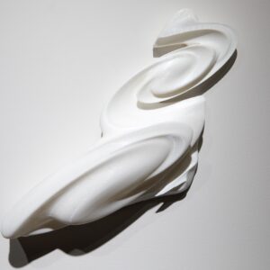 A white swoopy 3D printed piece installed against a white wall.