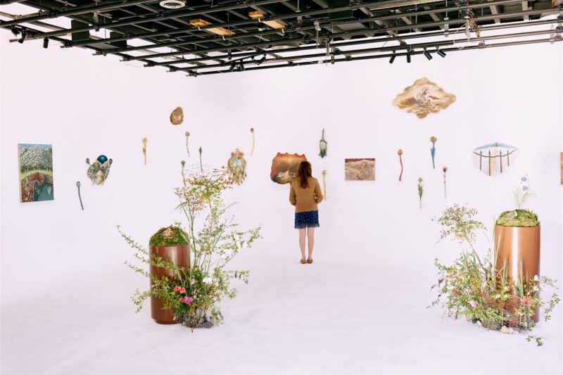 A woman with long dark hair stands among art installed on white walls and floor.