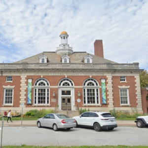 Street view of multistory brick building with arched windows and cupola.