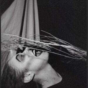 Black and white photograph of a person with dried branches against their face