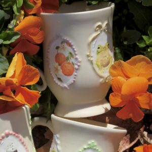 Three white ceramic mugs with intricate painting of images on them
