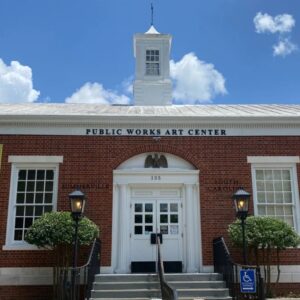 Multi-story brick building with white roof and cupola. Large white windows and doors. Five steps up to the entrance.